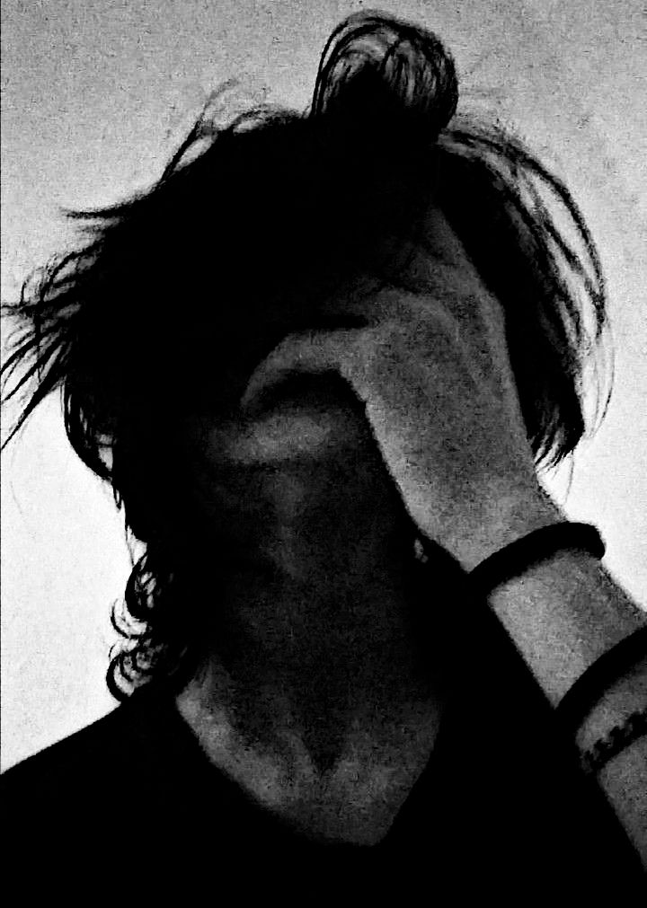 A monochrome image of a person with long hair, covering their face with one hand, expressing a sense of despair or frustration.